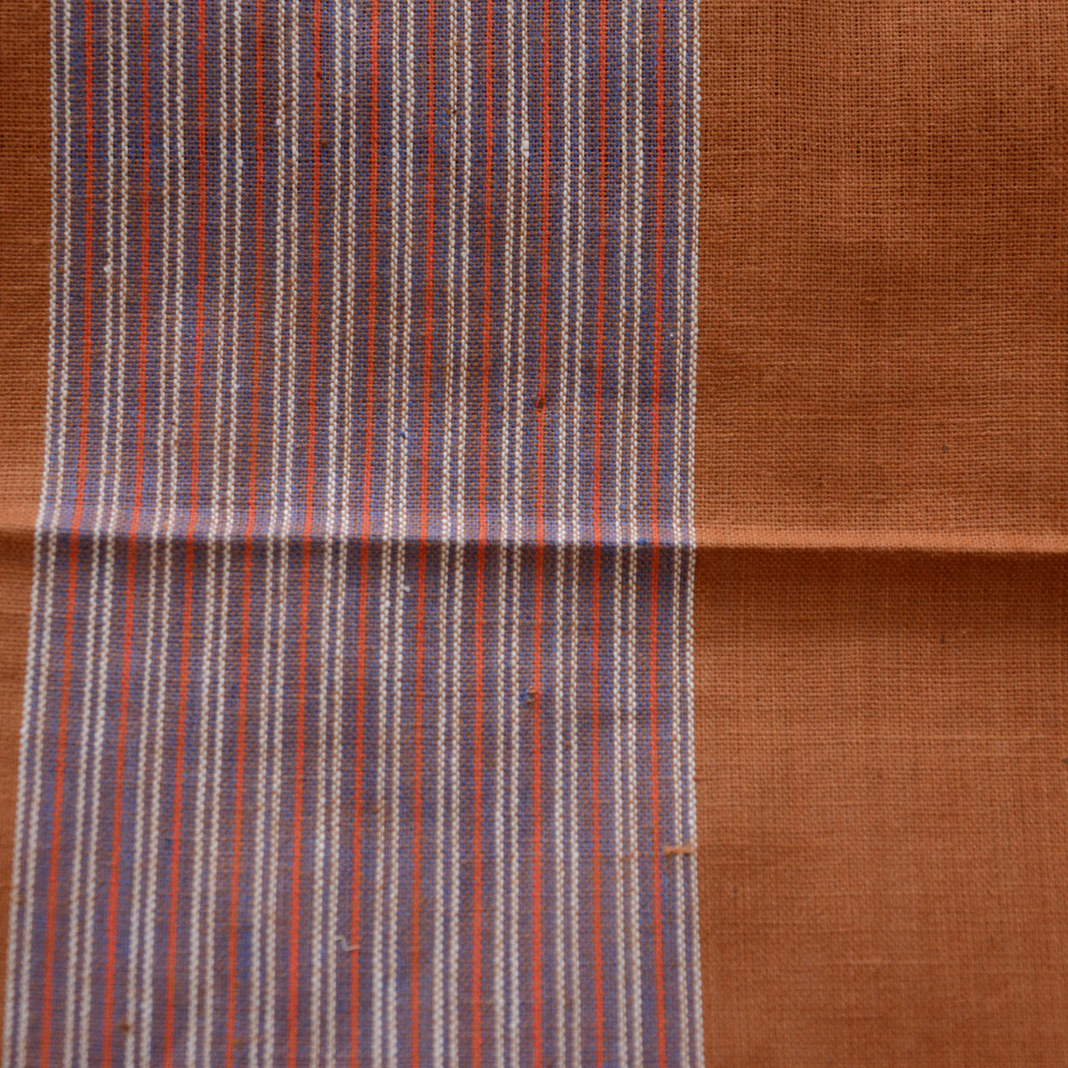 Small hole near the center of a purplish striped band on a brown cotton furoshiki