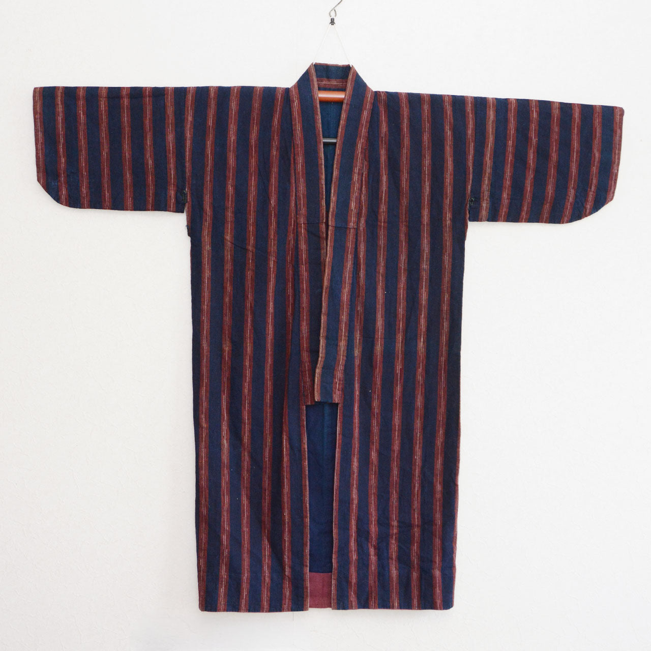 Vintage noragi jacket on hanger, front view — indigo-dyed cotton with wide-pitch red stripe, open-front construction, Tohoku, early Showa era