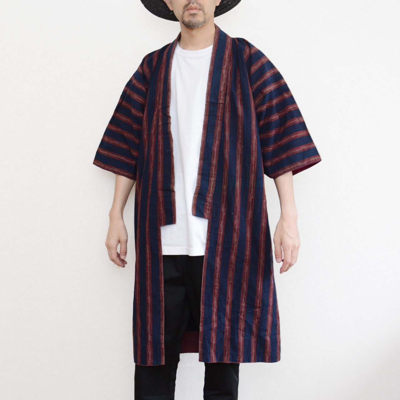 Vintage Japanese noragi jacket worn by a male model, front view — indigo-dyed cotton with bold red stripe, open-front wrap, tube sleeves, styled over white tee and black pants, Tohoku, early Showa era