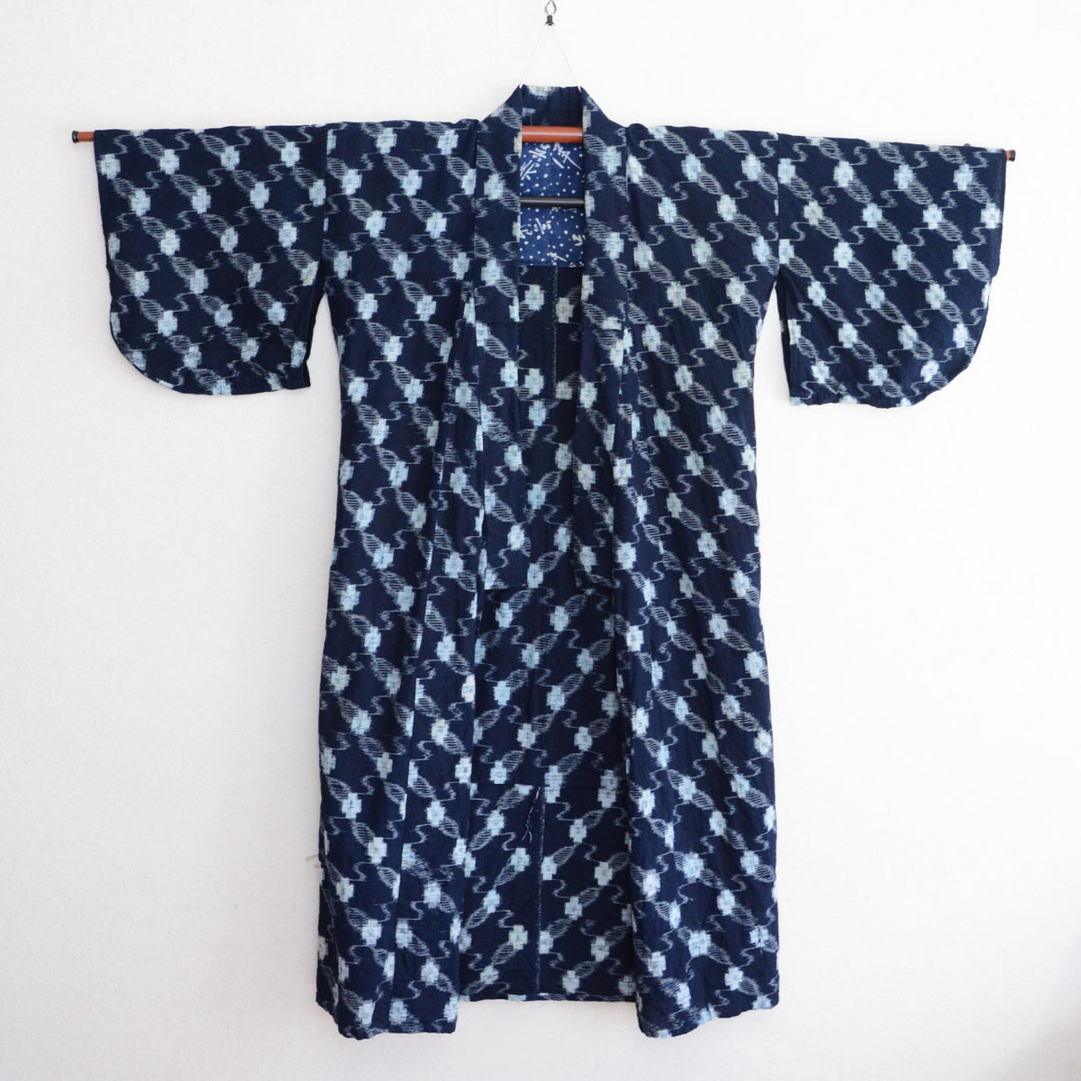Front view of a Japanese vintage indigo kasuri cotton kimono robe on a hanger, with the tenugui lining visible at the chest