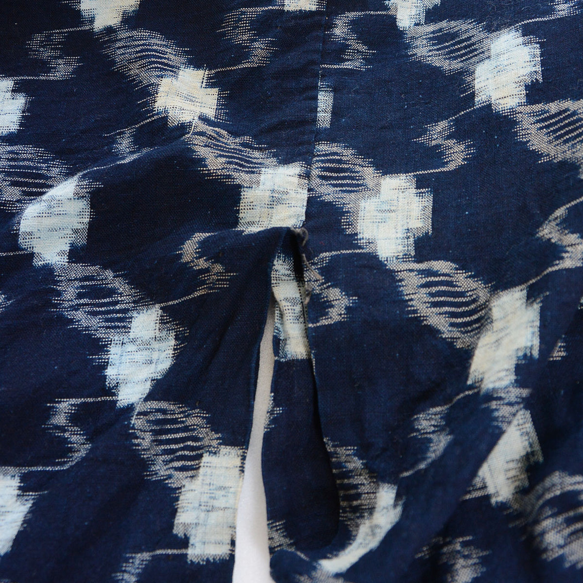 Close-up of the miyatsuguchi (underarm opening) of an indigo kasuri cotton kimono robe, showing partially missing stitches