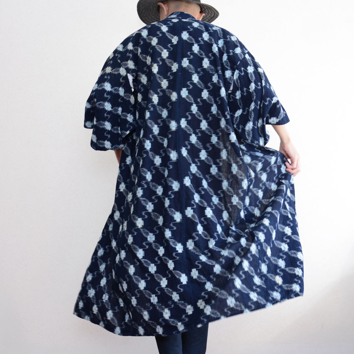 Back view of a male model wearing an indigo kasuri cotton kimono robe, holding out the hem