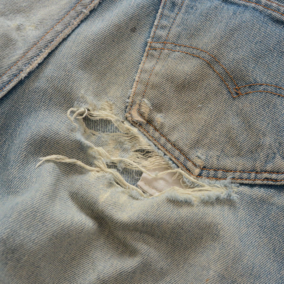 Levi’s 501 faded blue denim with a tear and frayed white threads below the right rear pocket