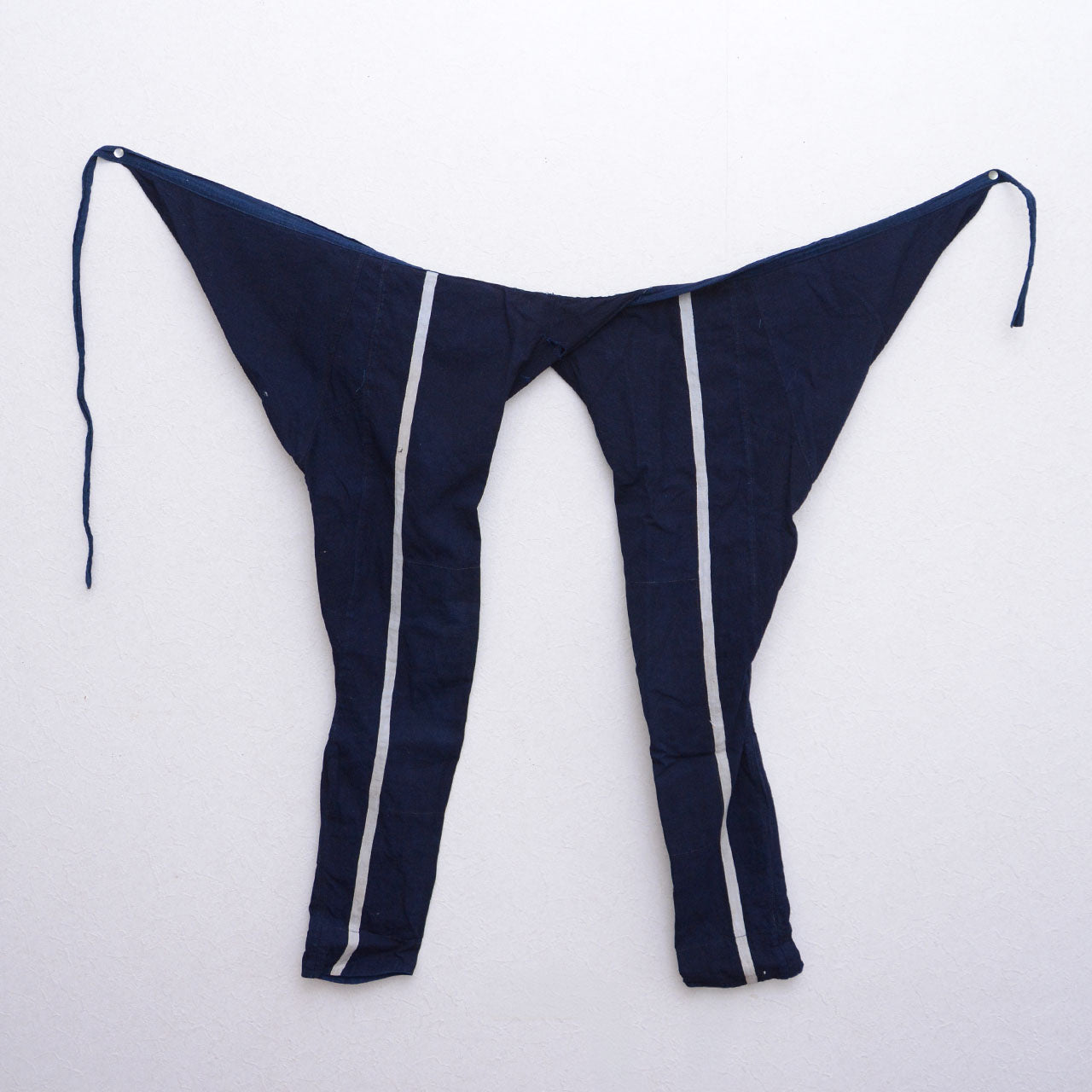 Indigo cotton momohiki displayed on a wall, with natural-colored stripe detail visible on the legs