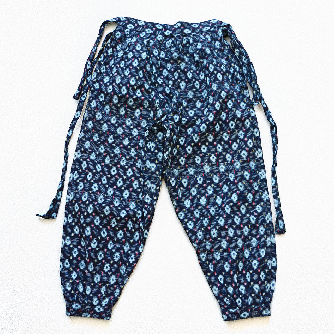 indigo kasuri cotton monpe — navy ground with light blue ikat motifs and multicolor accent threads, front view with tie waist