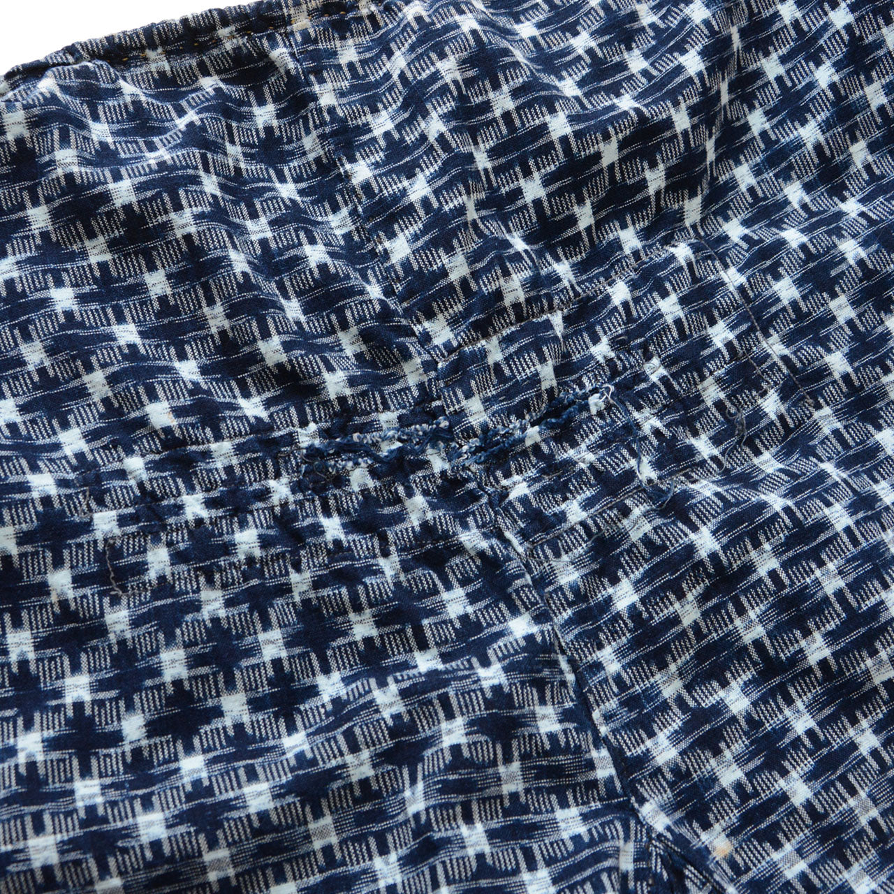Repair area of indigo kasuri monpe pants, exterior view, hand-stitched mend on navy ikat check cotton, Japan vintage