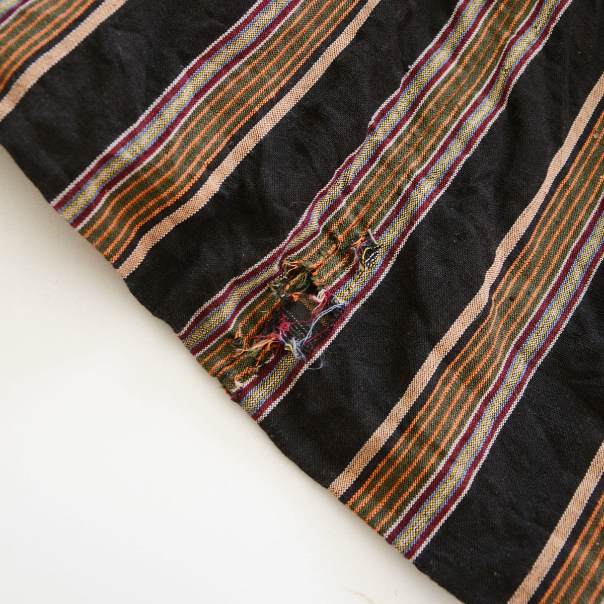 Tear and frayed threads in the striped cotton of a vintage noragi