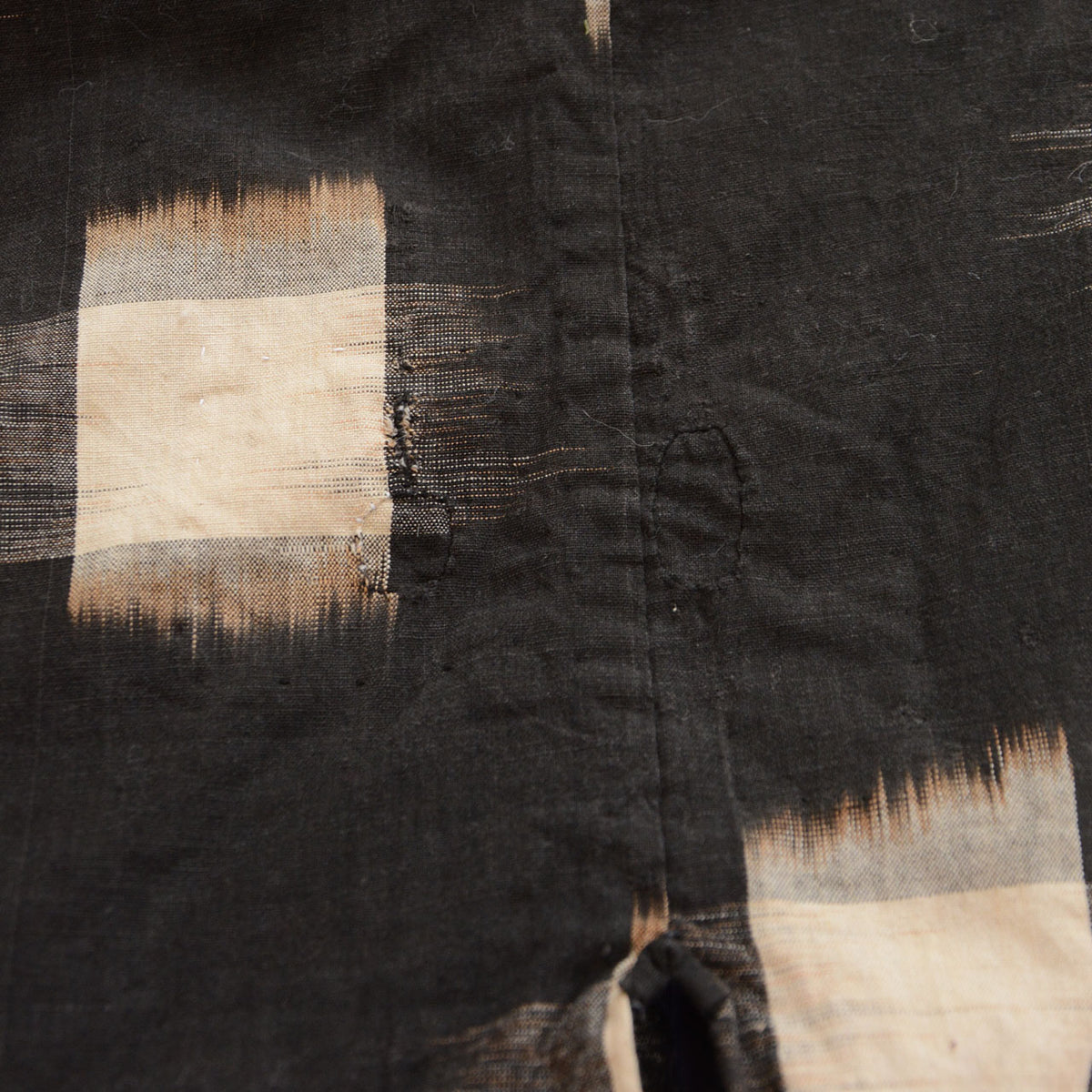 Fine dark-thread repairs beside a seam and ecru kasuri motif on cotton noragi fabric.