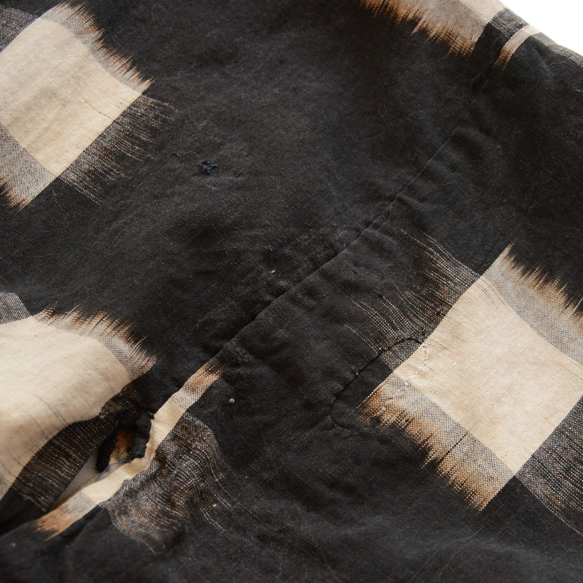 Small mended areas and dark stitches across vintage cotton kasuri fabric.