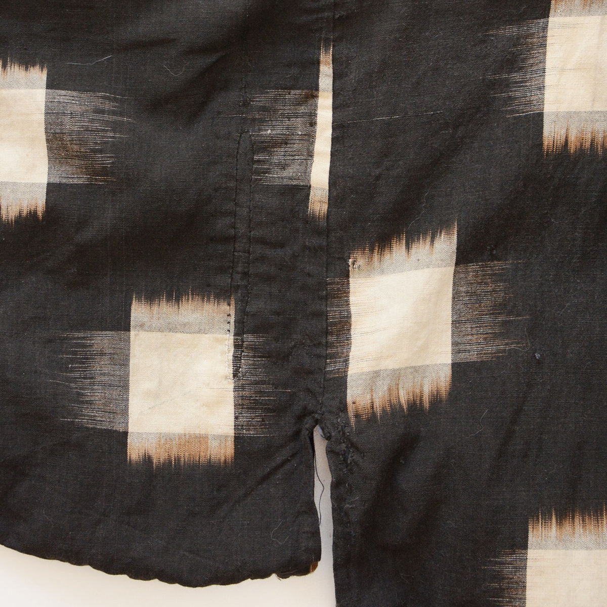 Elongated mended area beside an opening in dark cotton with ecru kasuri motifs.