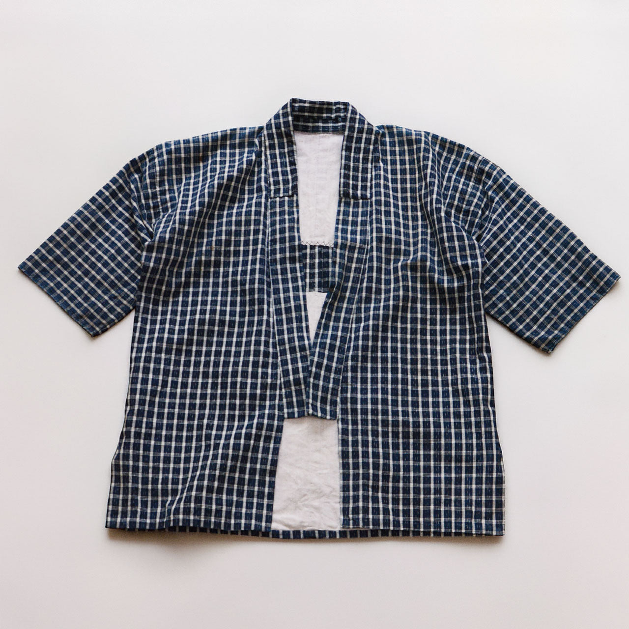 Vintage noragi jacket laid flat, front view — indigo-dyed cotton check, open-front wrap construction, early Showa era Japan vintage