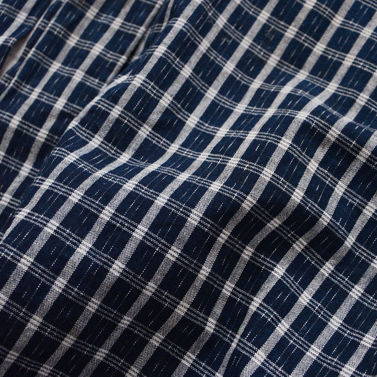 Close-up of indigo-dyed cotton check weave — vintage noragi fabric showing grid pattern, natural fade, and hand-woven textile texture, early Showa era Japan vintage