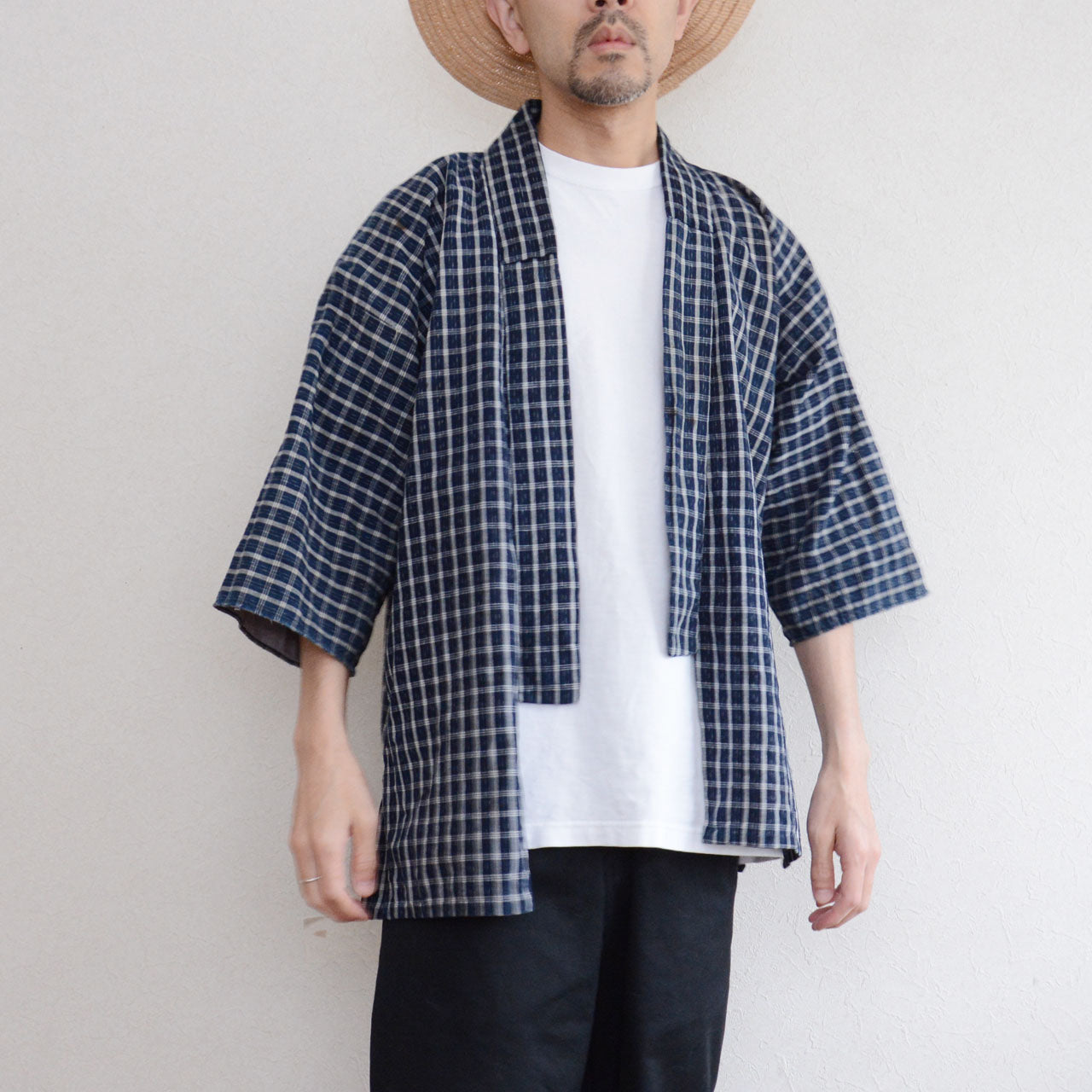 Vintage noragi jacket worn by a male model, front view — indigo-dyed cotton check, open-front wrap, styled over white tee and black pants, straw hat, early Showa era Japan vintage