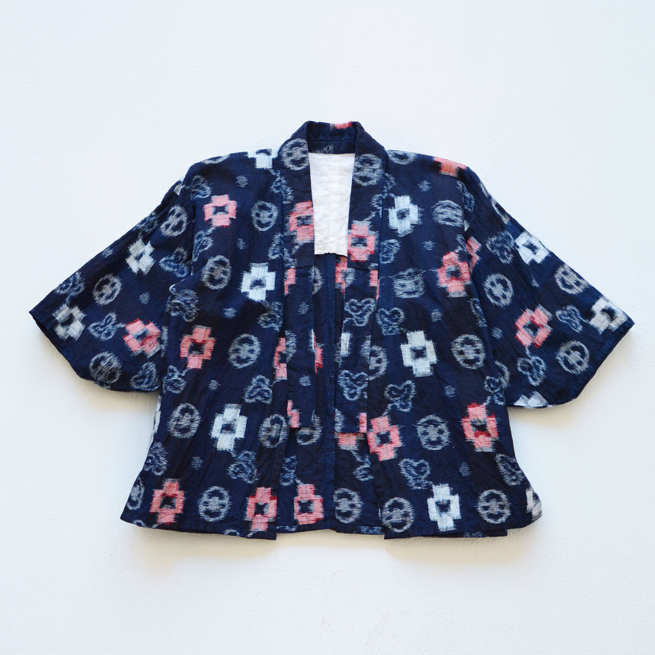 Indigo-dyed cotton noragi jacket, e-gasuri ikat weave, navy ground with multi-motif kasuri pattern in white and red, laid flat front view, Japan vintage