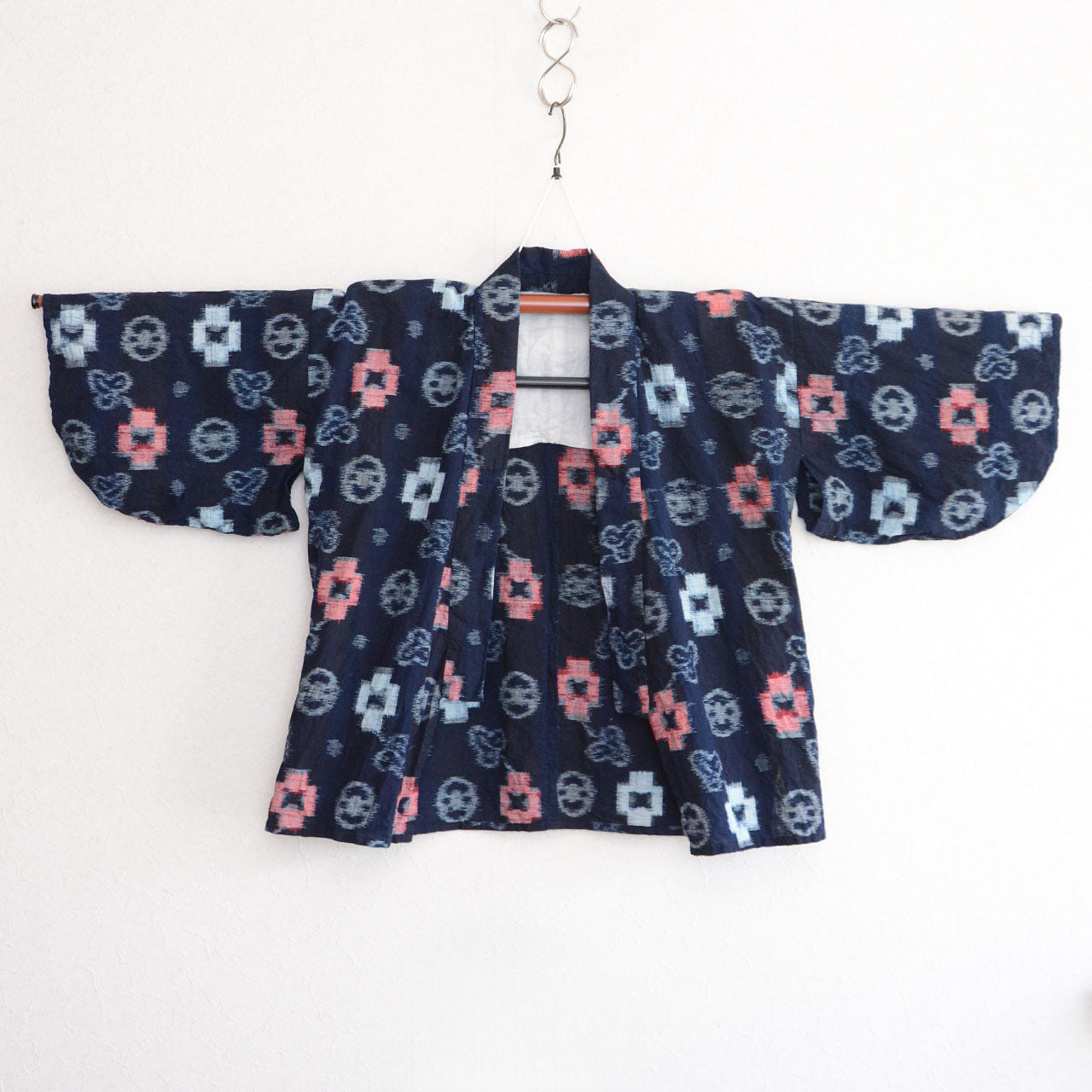 Indigo-dyed cotton noragi jacket, e-gasuri ikat weave, navy ground with multi-motif kasuri pattern in white and red, front view on kimono hanger, Japan vintage