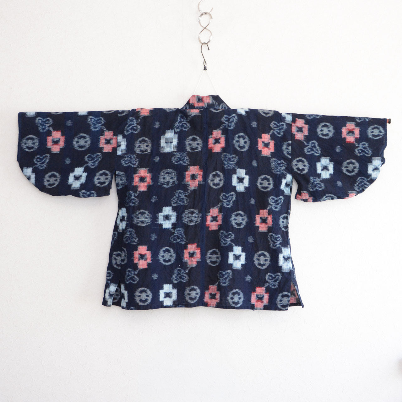 Indigo-dyed cotton noragi jacket, e-gasuri ikat weave, navy ground with multi-motif kasuri pattern in white and red, back view on kimono hanger, Japan vintage
