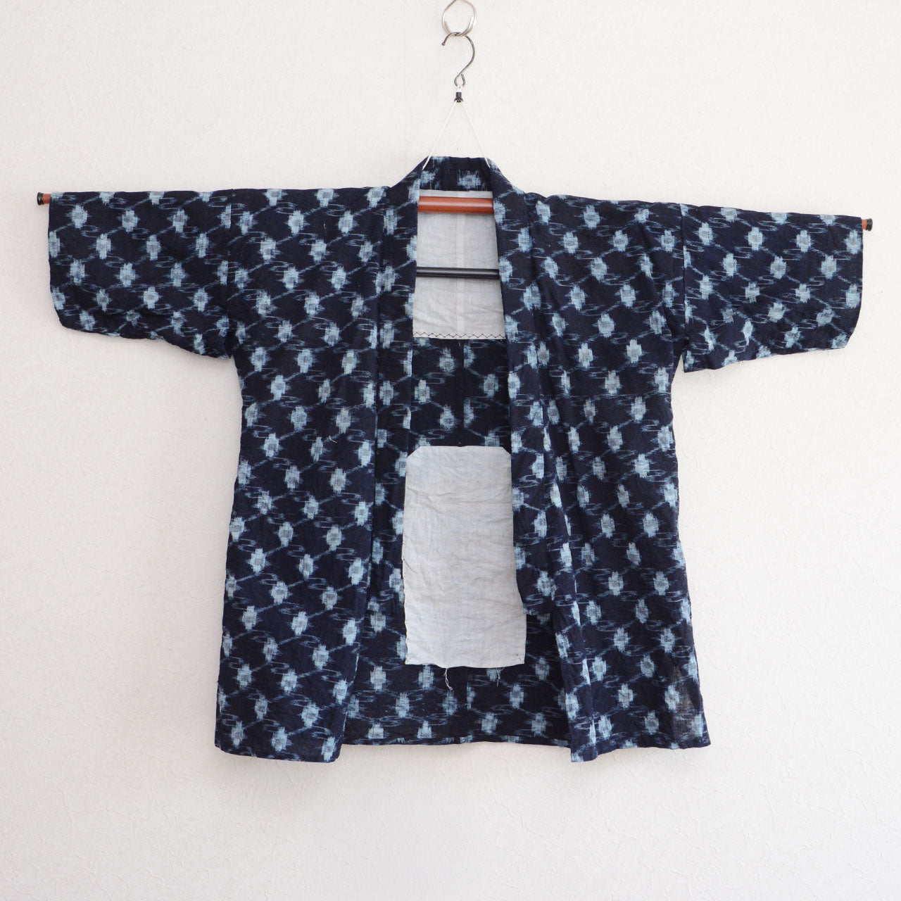 Indigo kasuri cotton noragi jacket, navy, diamond ikat pattern, open front, white cotton lining visible, Showa era Japan vintage, on hanger