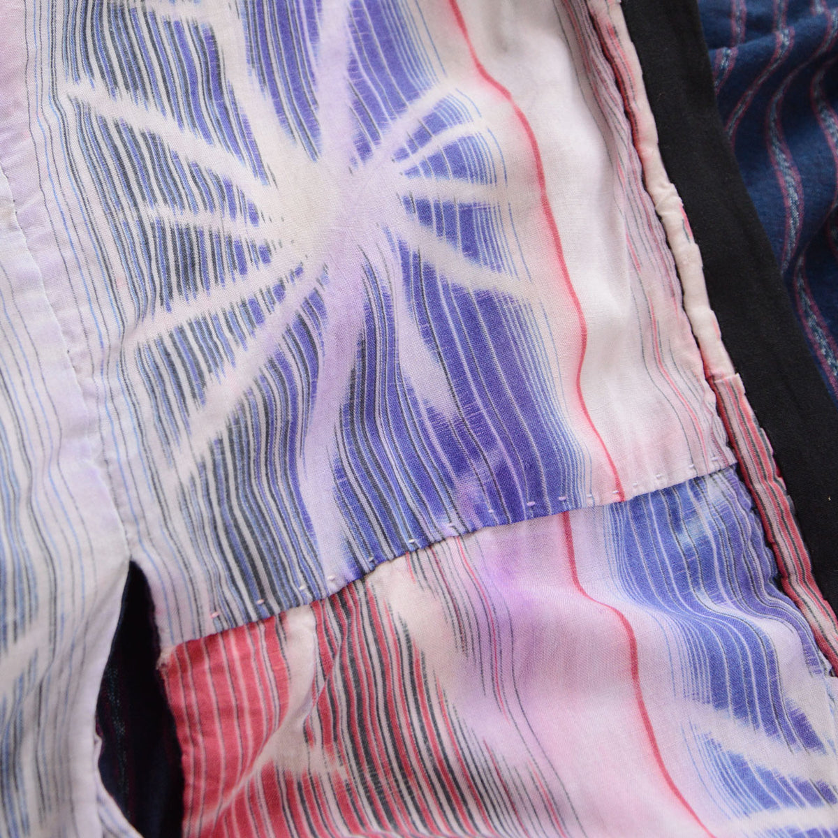 Close-up of pink and blue patterned cotton with holes, fraying, and color bleeding on a Japanese vintage noragi jacket