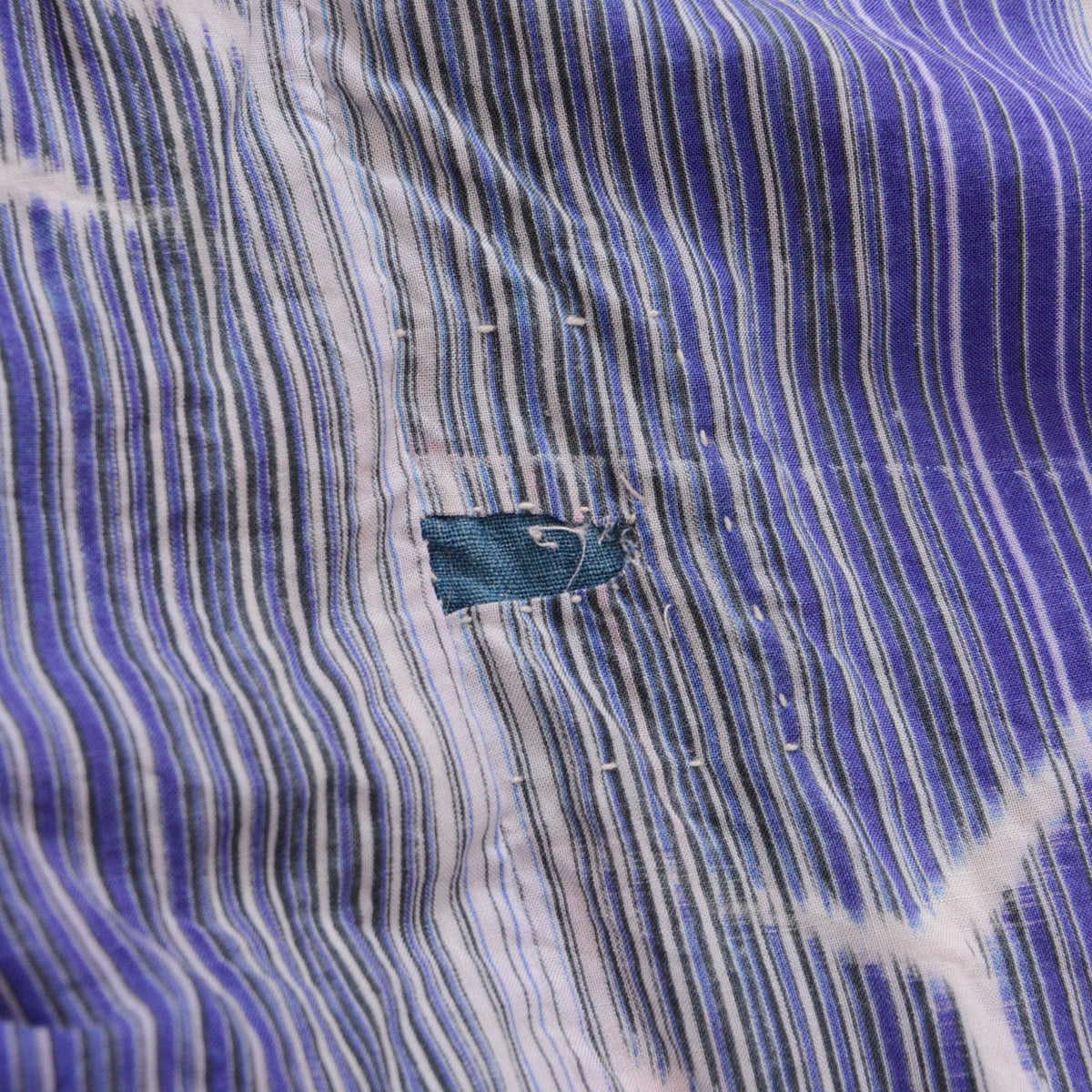 Close-up of a repaired area on indigo striped cotton with visible stitching on a Japanese vintage noragi jacket