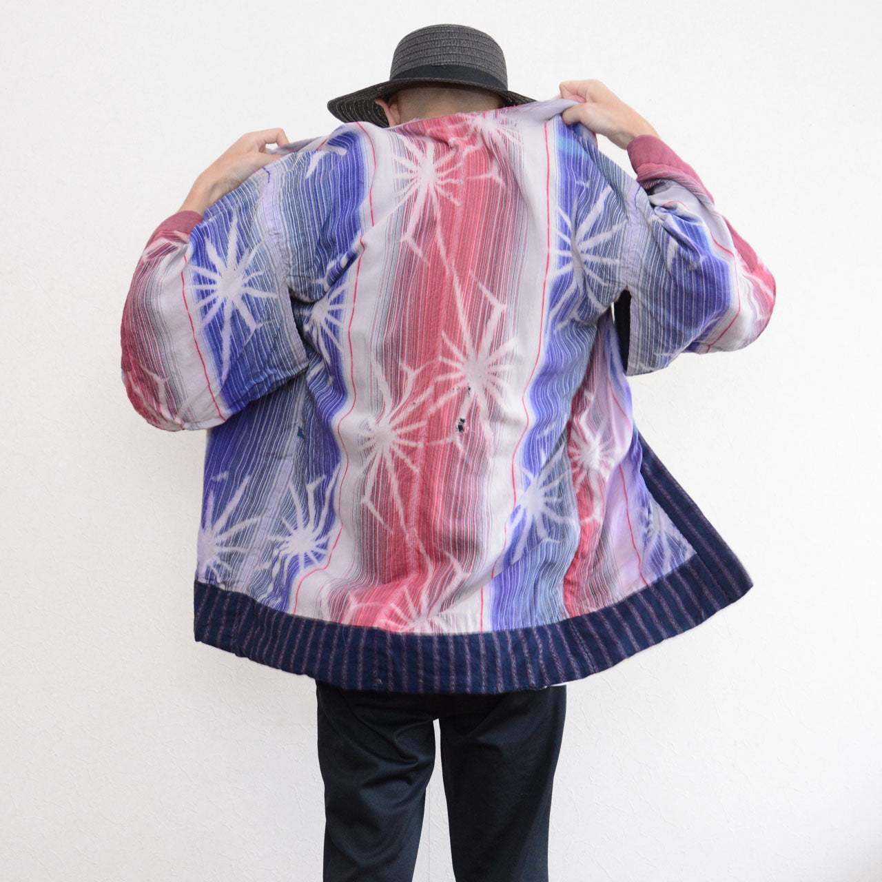 Back view of a model wearing a Japanese vintage noragi jacket with pink, blue, and white patterned cotton and an indigo striped hem