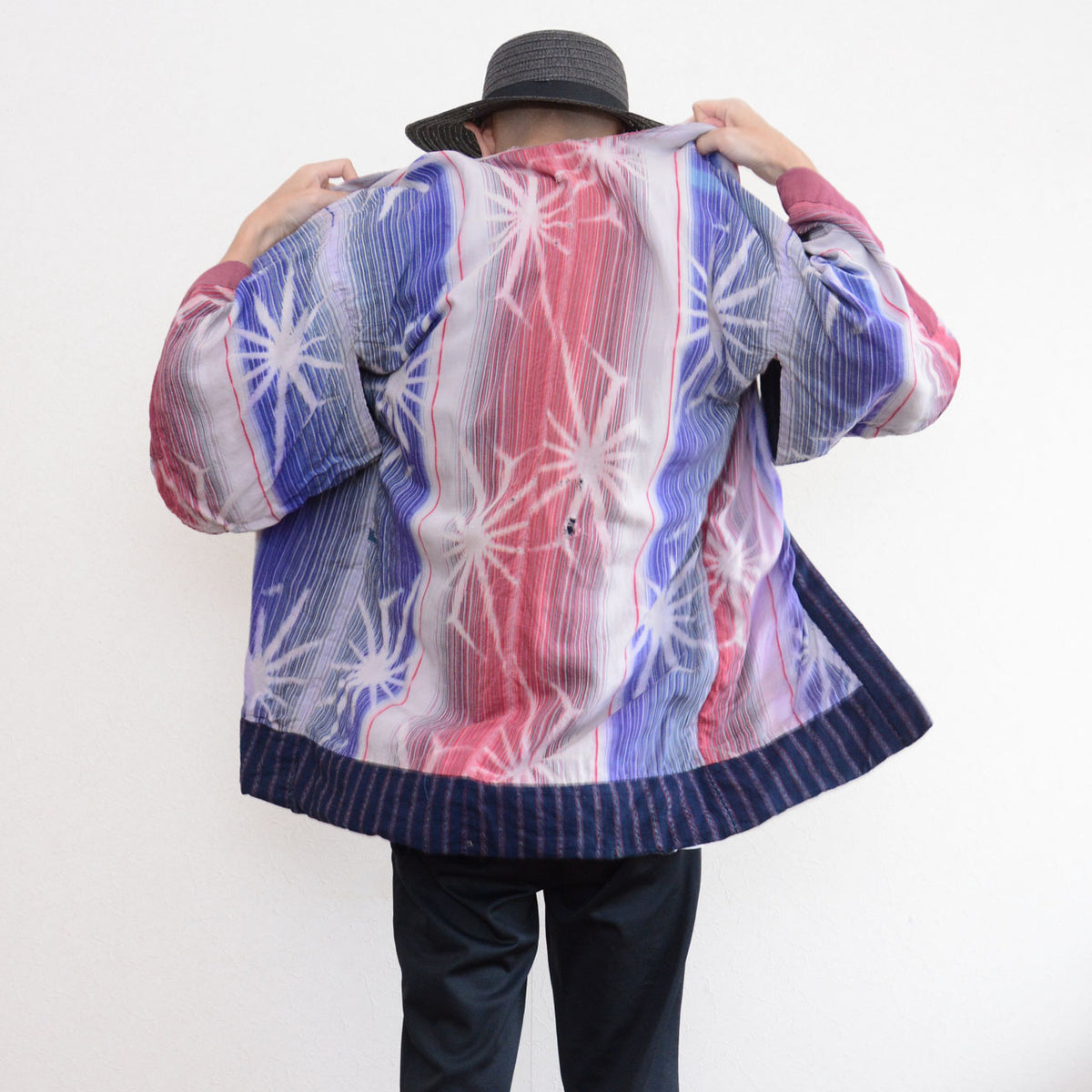 Back view of a model wearing a Japanese vintage noragi jacket with pink, blue, and white patterned cotton and an indigo striped hem