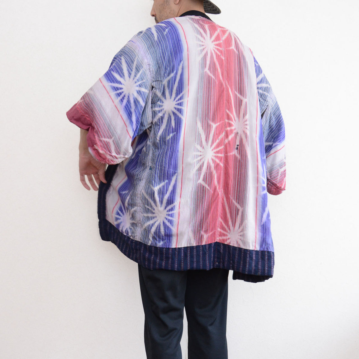 Back three-quarter view of a model wearing a Japanese vintage noragi jacket with colorful patterned cotton panels and an indigo striped hem