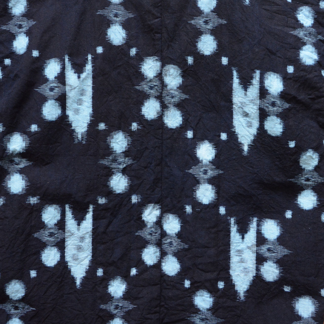 Close-up of indigo kasuri cotton fabric showing abstract dot and geometric ikat pattern, vintage Japanese noragi jacket