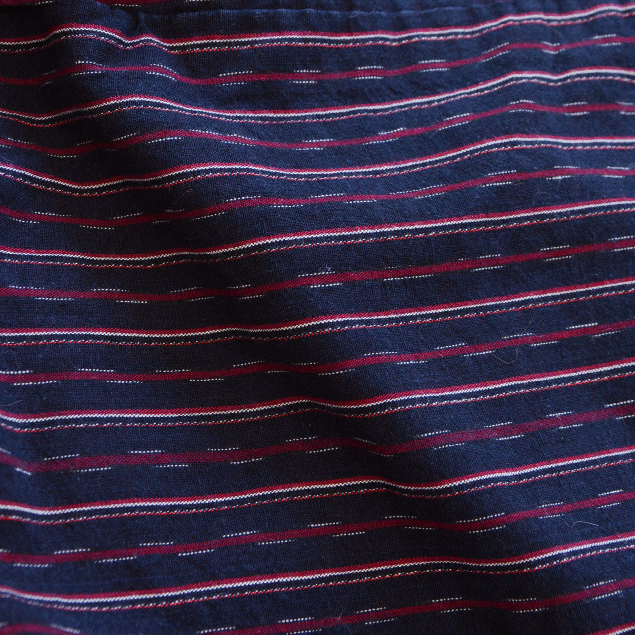 Close-up of navy cotton stripe fabric texture, maroon and white stripe on indigo ground