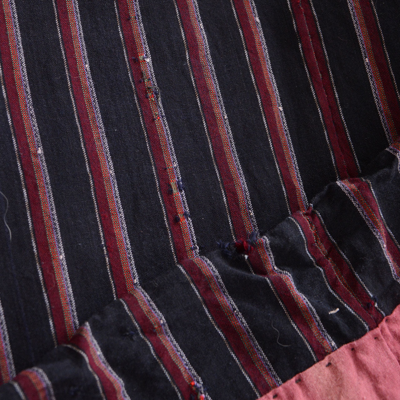 Japanese noragi with repaired and frayed red and gray striped cotton fabric and a salmon-pink lining visible at the lower edge