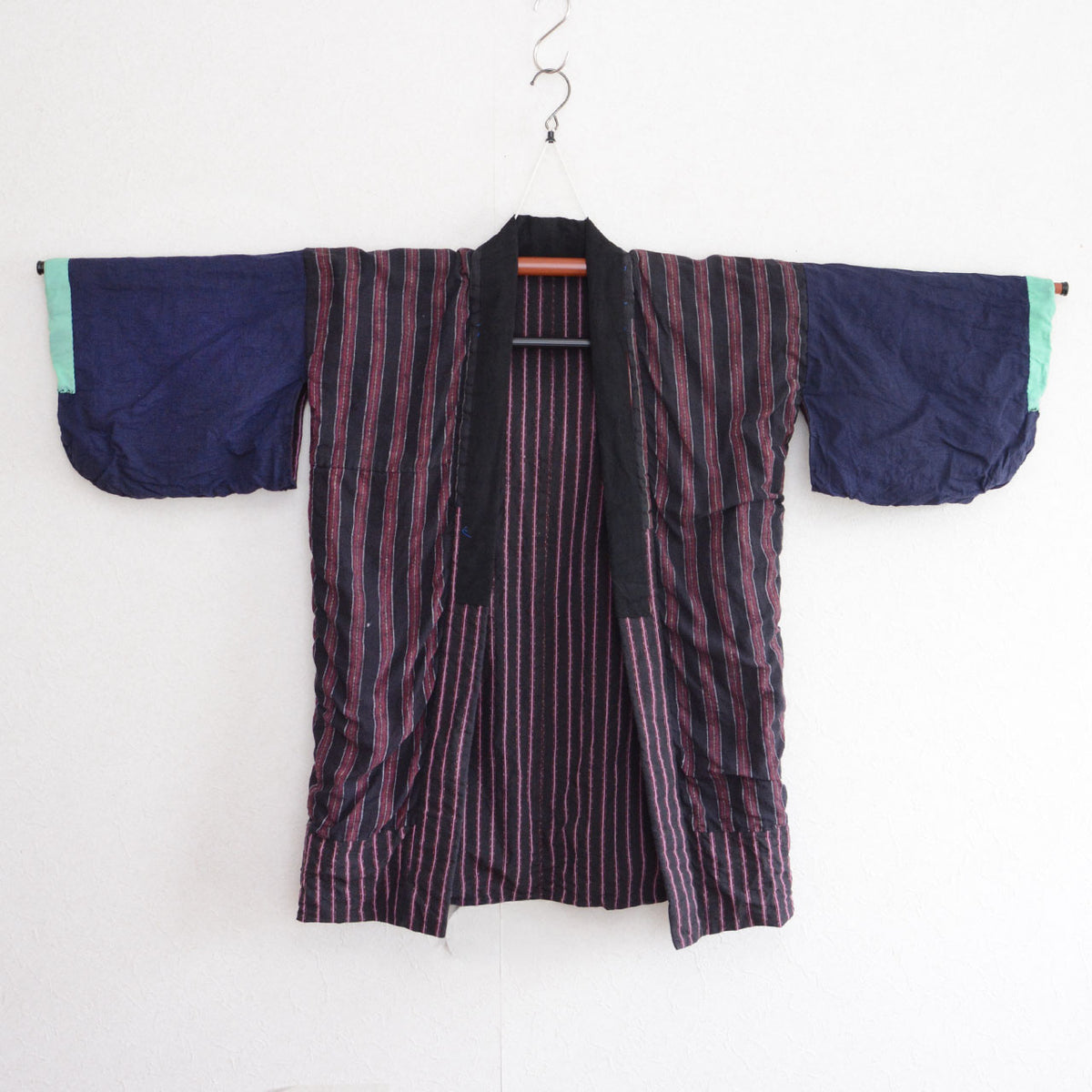 Front of a Japanese vintage cotton noragi on a kimono hanger, with a striped body, solid navy sleeves, and mint-green cuffs