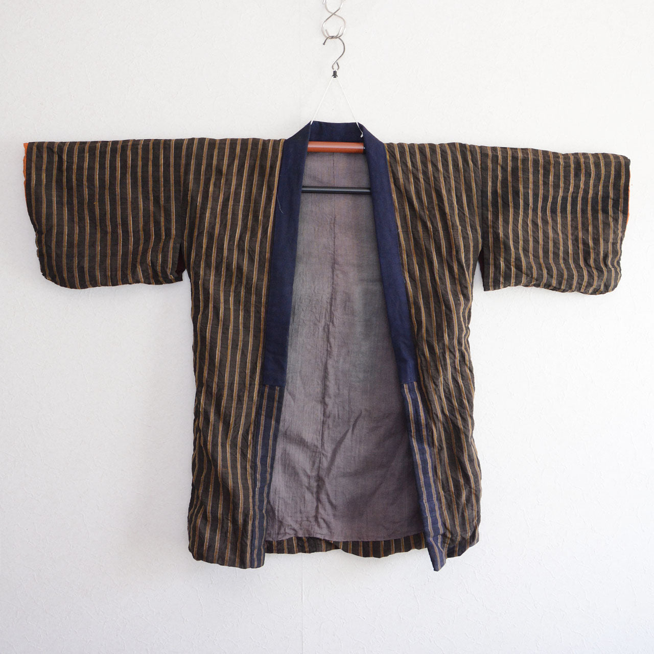 Vintage Japanese noragi jacket, Showa era, dark brown and navy vertical stripe outer fabric, gray lining visible at front opening, hanging view