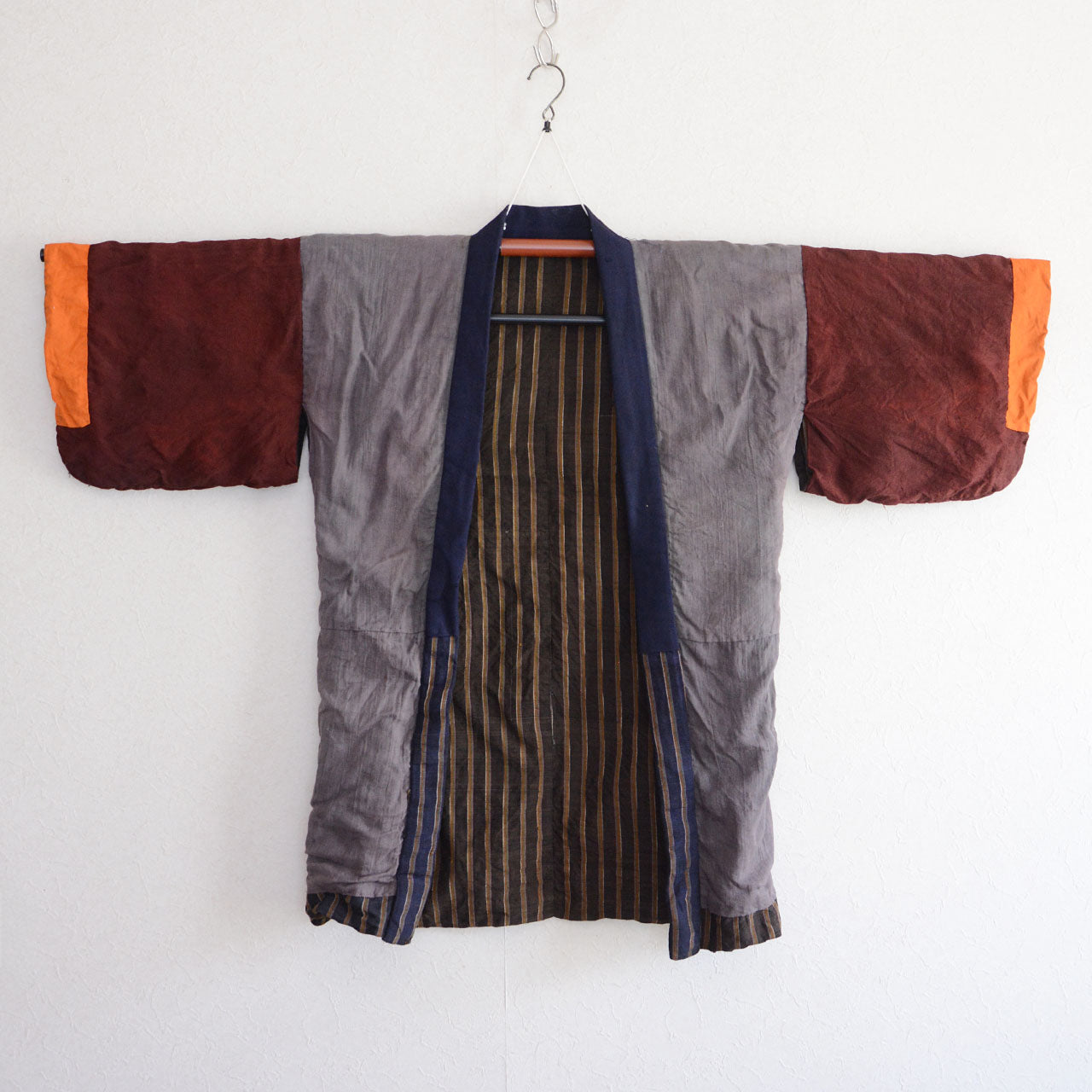 Vintage Japanese noragi jacket, Showa era, gray mixed fabric body, burgundy and orange patchwork sleeves, dark vertical stripe lining visible at front opening, hanging view
