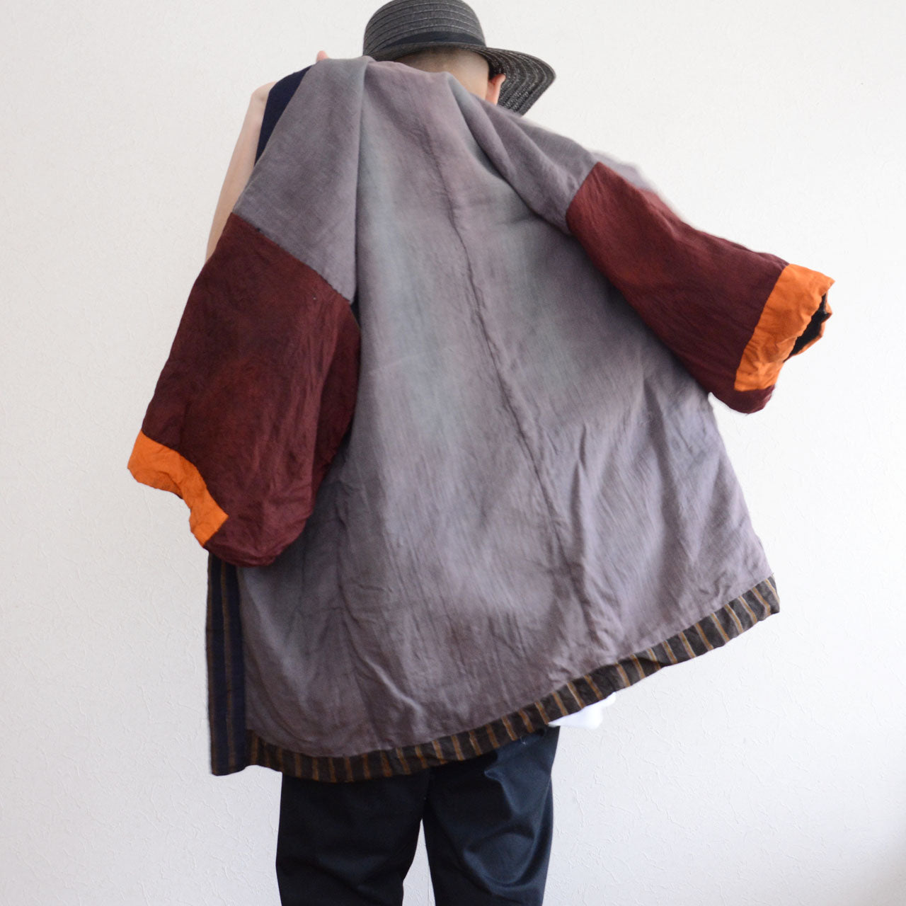 Vintage Japanese noragi jacket, Showa era, gray mixed fabric body with burgundy and orange patchwork sleeves, back view with wide kimono sleeves spread open, multicolor stripe lining visible at hem, model height 171cm