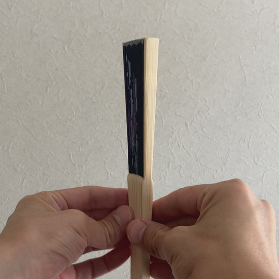 Hand slowly unfolds traditional sensu fan with delicate morning glory pattern