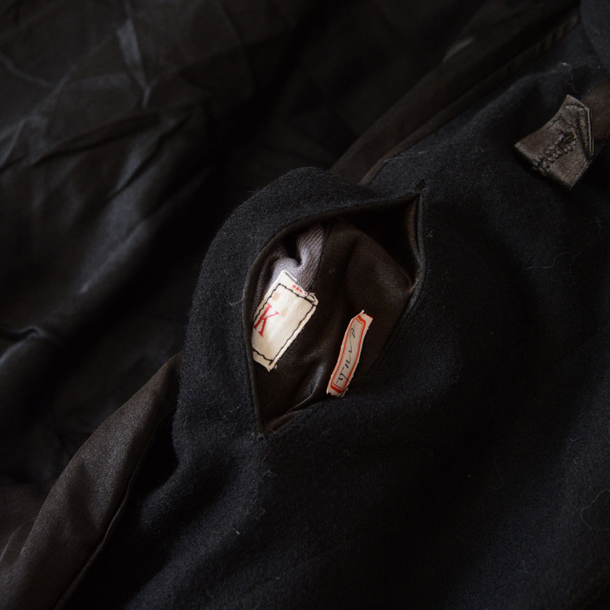 Two white fabric labels inside an additional small pocket of a Matsuzakaya black wool Japanese vintage tonbi coat